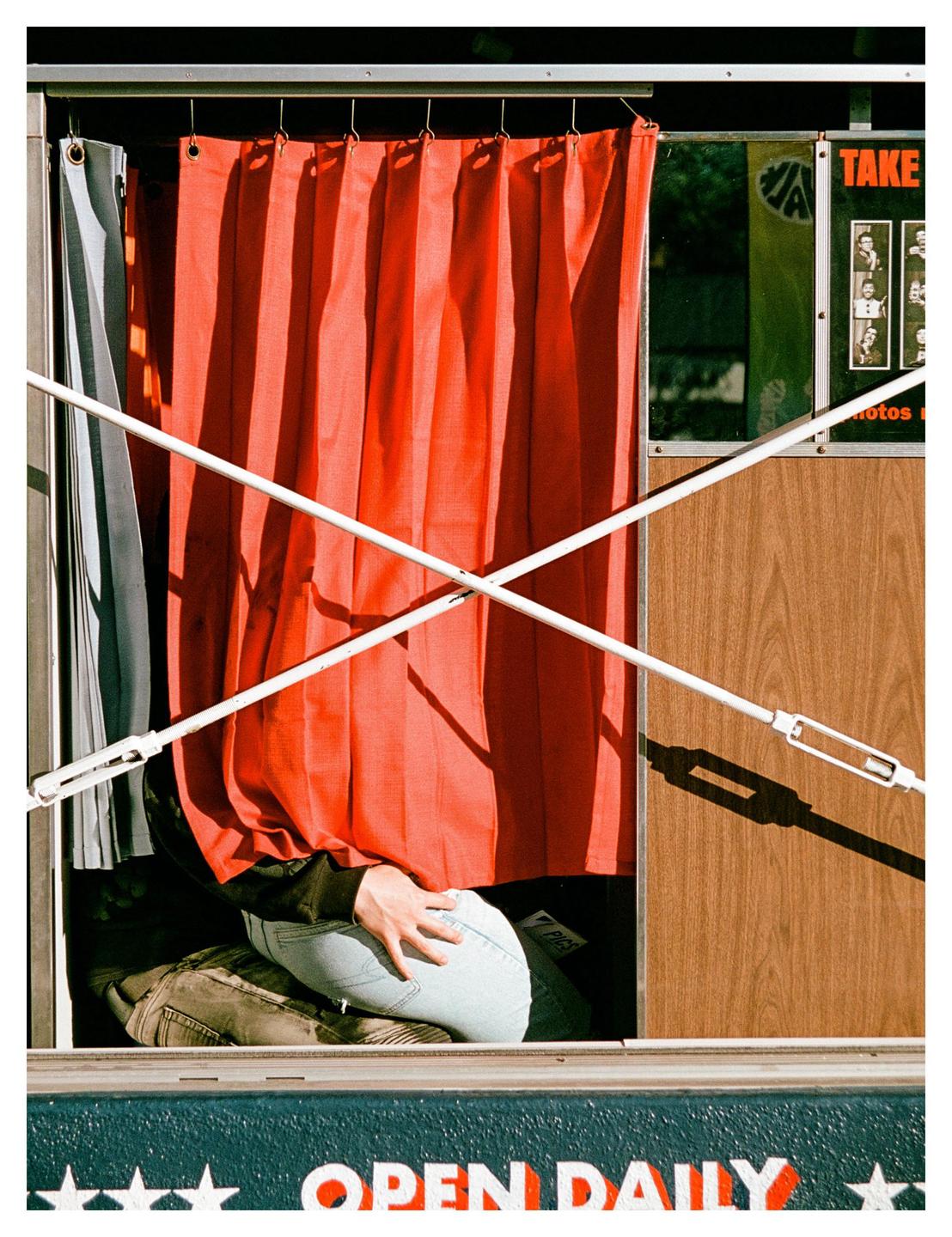 A person is visible from the waist down inside a photo booth with a red curtain.