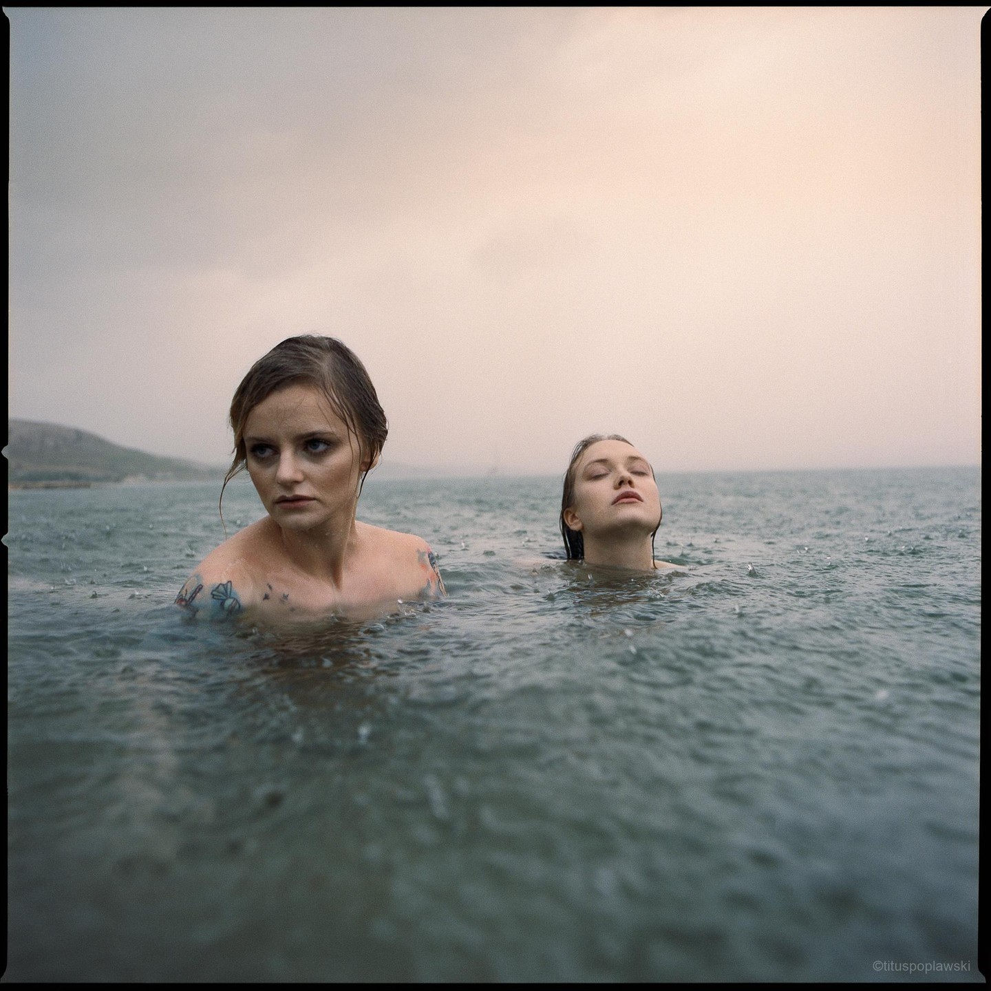Two women are in the water with rain falling around them.