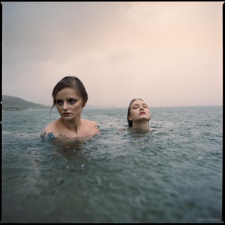 Two women are in the water with rain falling around them.