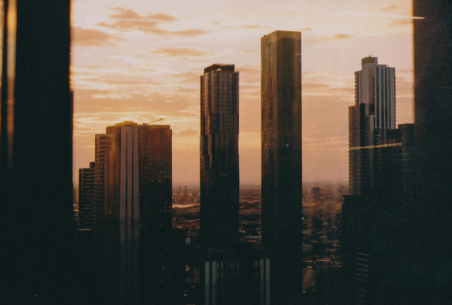 A city skyline with several tall buildings is silhouetted against a cloudy, orange sky at dusk.