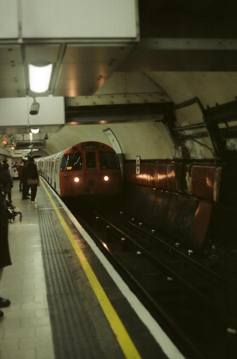 A red and white train approaches a subway platform where people are waiting.