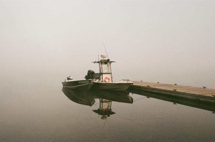 A boat is docked next to a pier on a hazy lake.