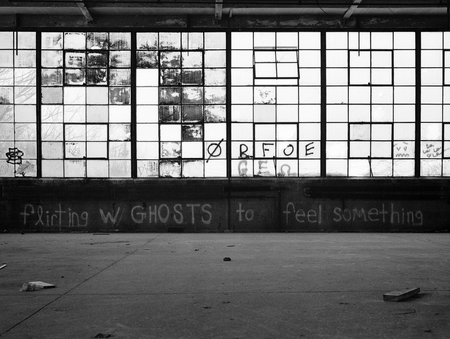 A large window with many panes, some broken, has graffiti on the glass and on the wall below it.