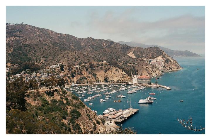 A wide shot shows a harbor full of boats and a town built into a steep hillside.