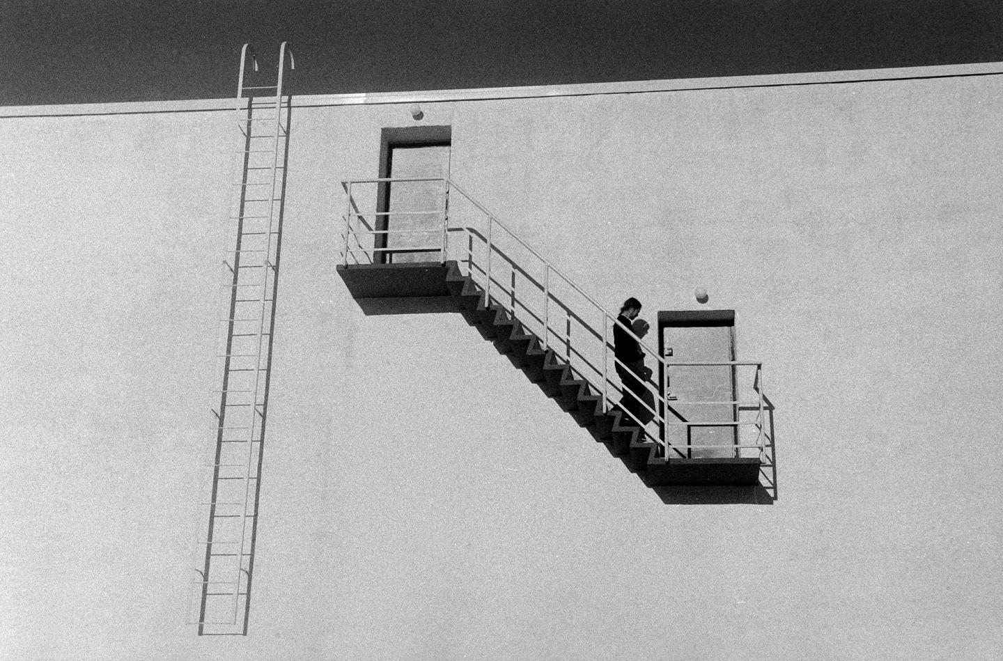 A woman descends an outdoor staircase on the side of a building, next to a tall ladder.