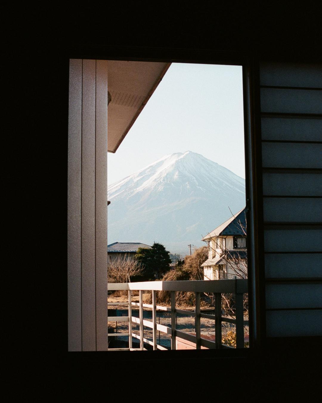 A snow-capped mountain is visible through an open window with a balcony and houses in the foreground.
