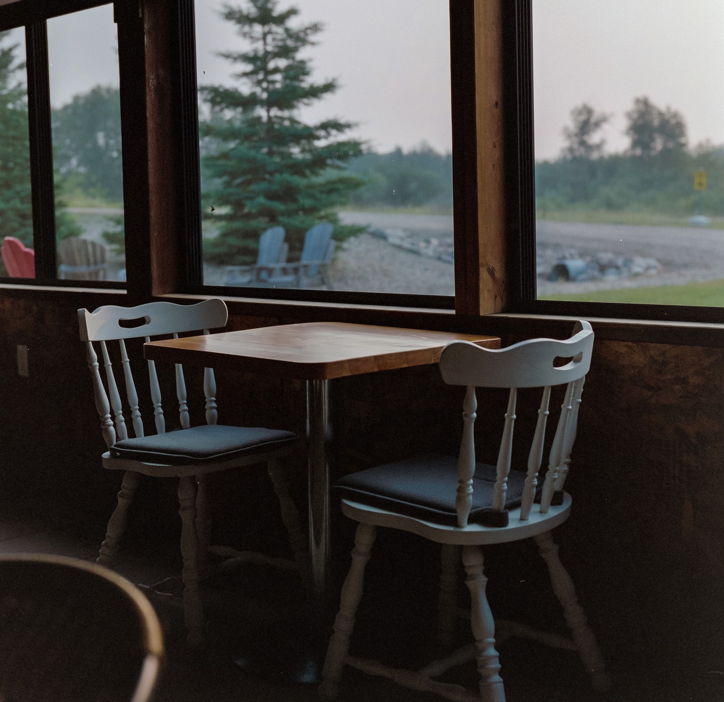 Two chairs and a table are visible through a window looking out onto a hazy landscape with trees and a road.