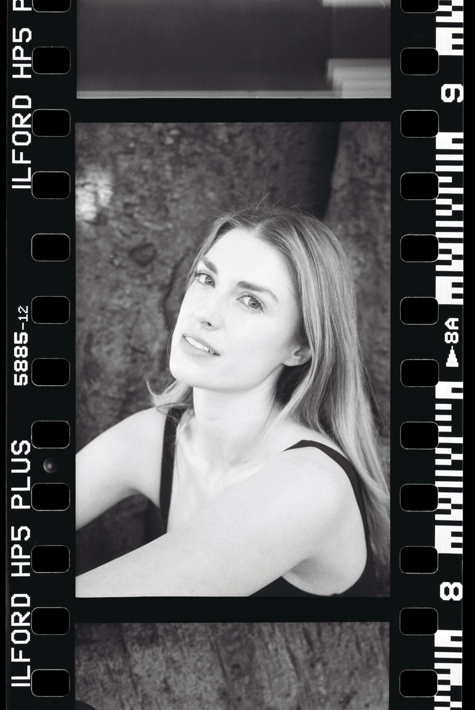 A woman with long hair looks towards the camera, framed by the sprocket holes and edge markings of a film strip.