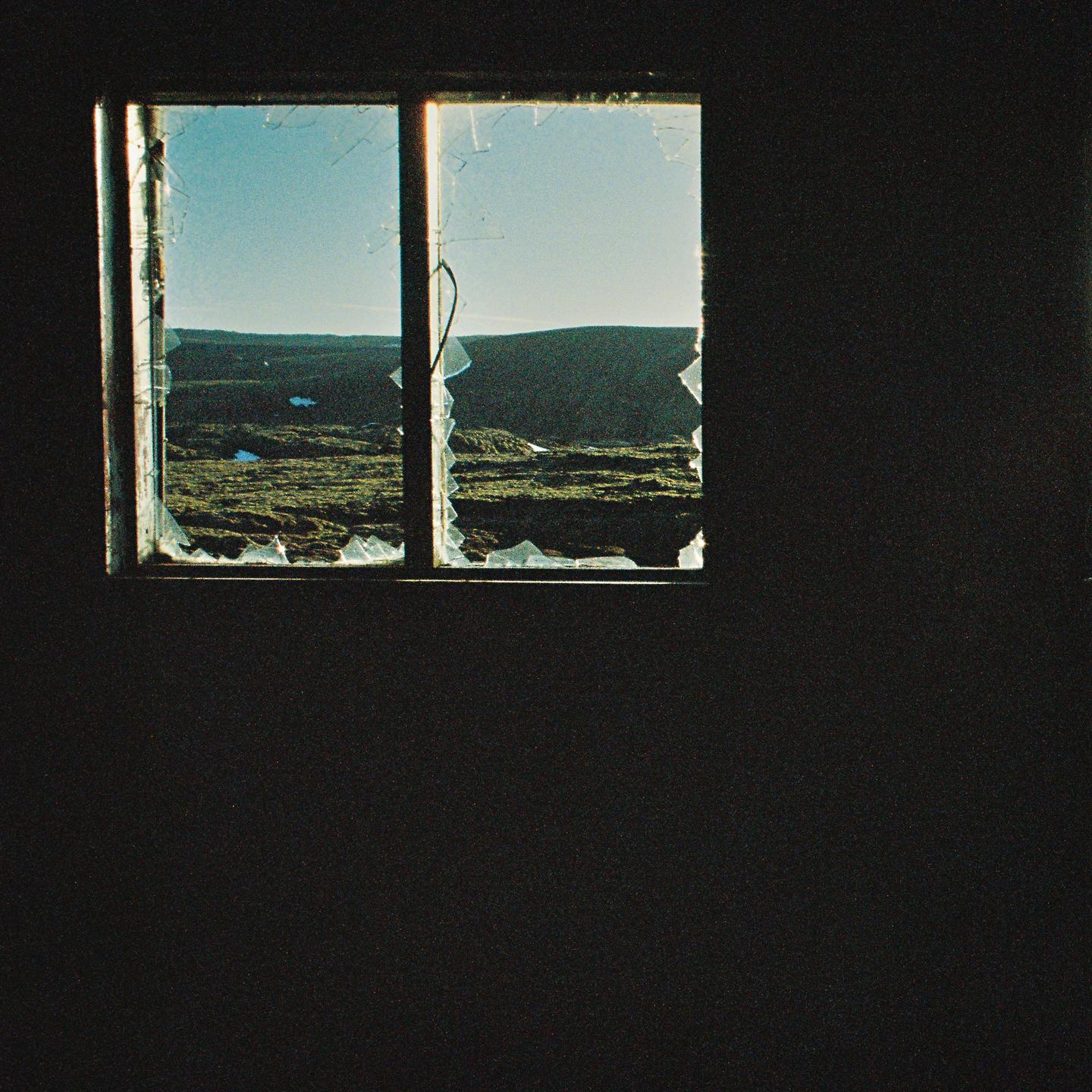 A broken window looks out onto a vast, mossy landscape under a clear sky.