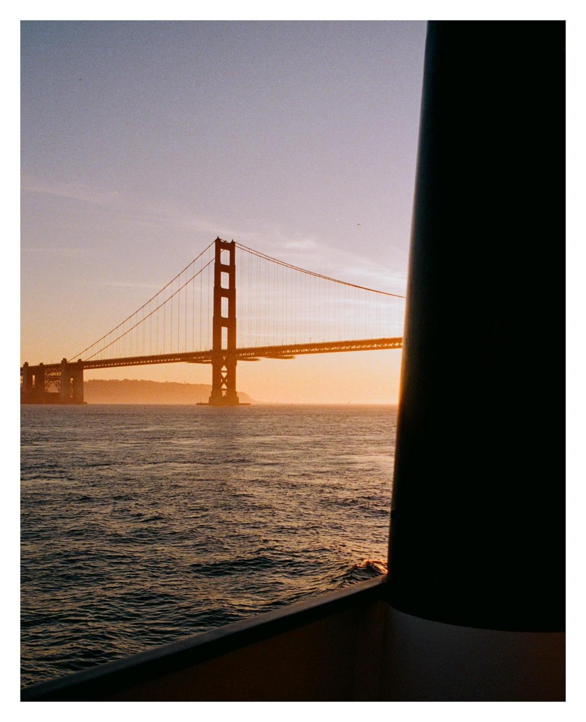 The Golden Gate Bridge is visible from a boat on the water at sunset.
