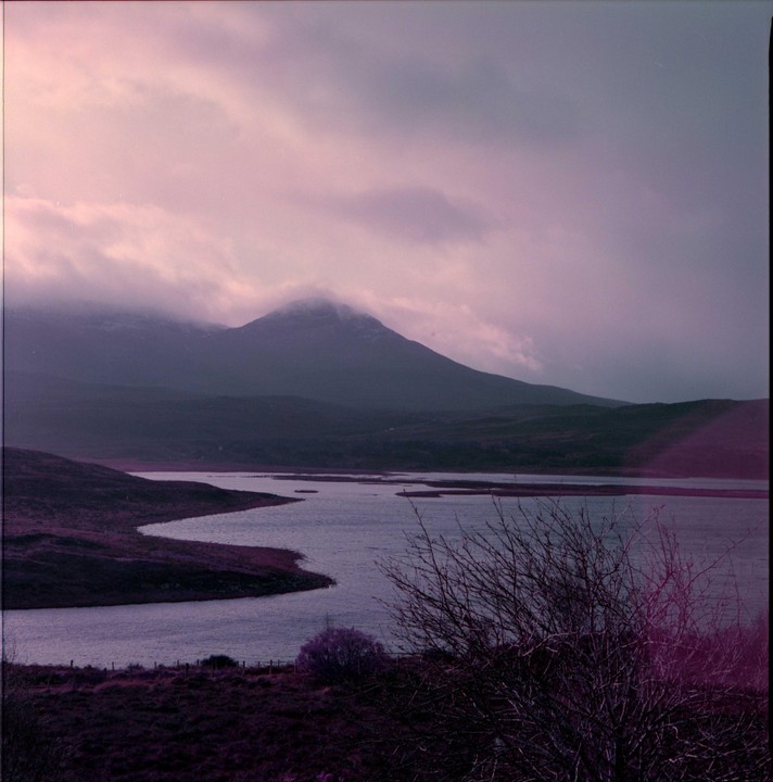 A winding body of water is visible in a mountainous landscape under a cloudy sky.