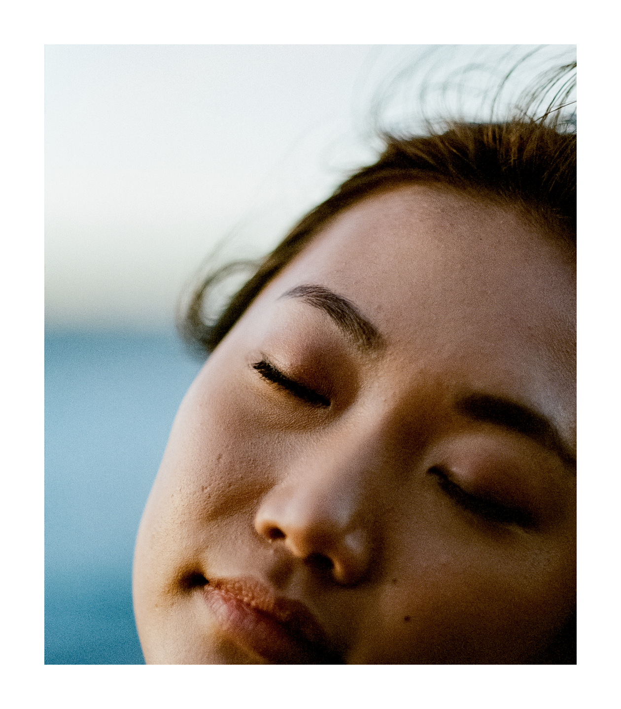 A woman's face with closed eyes is shown in a close-up portrait with a blue background.