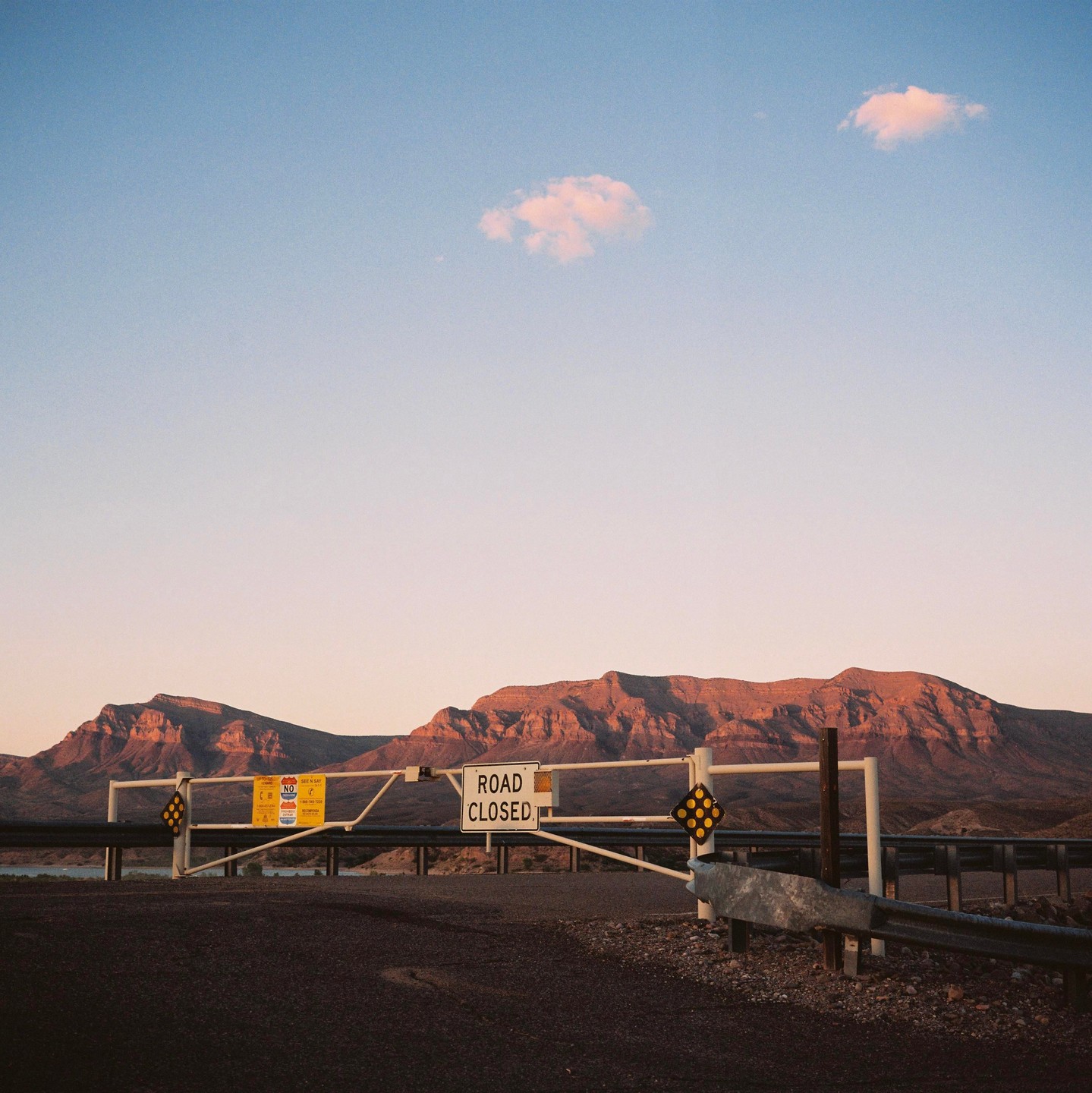 A "road closed" gate stands in front of mountains under a clear sky.
