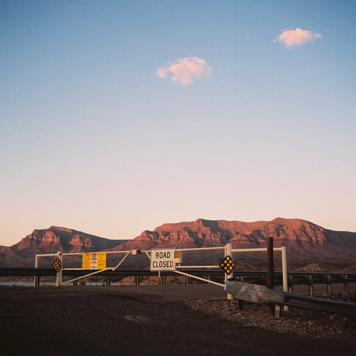 A "road closed" gate stands in front of mountains under a clear sky.