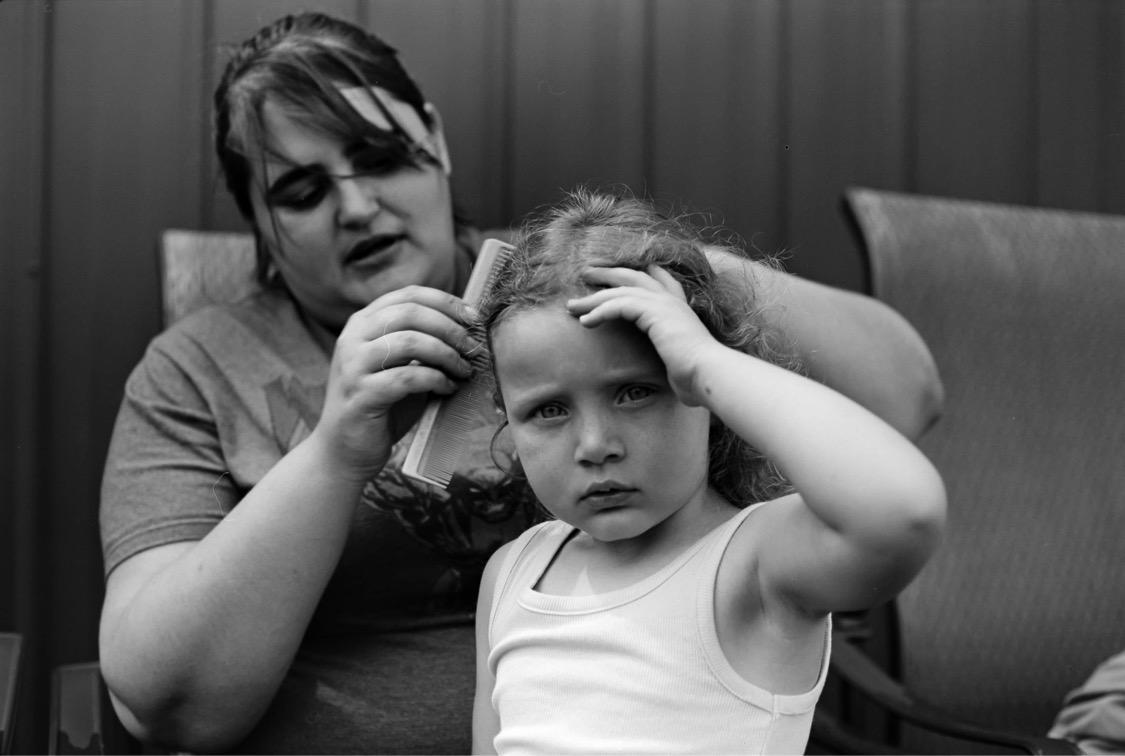 A woman combs the hair of a child who is looking directly at the viewer.
