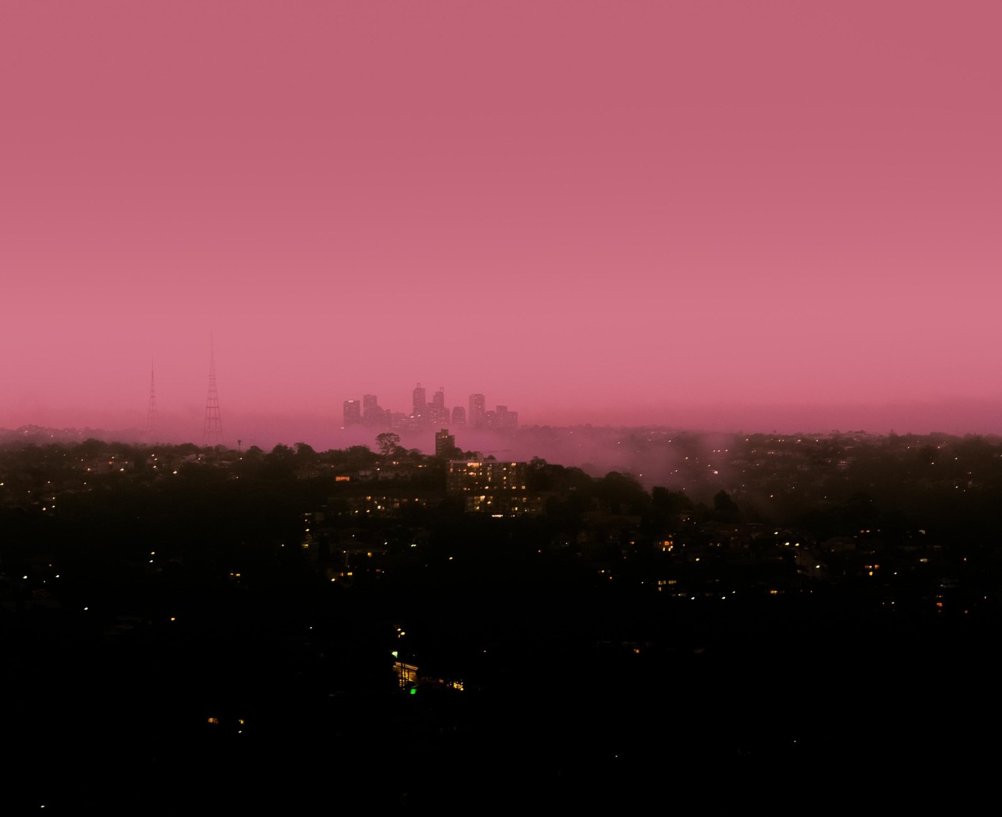 A city skyline is visible through a thick layer of fog under a vibrant pink sky.