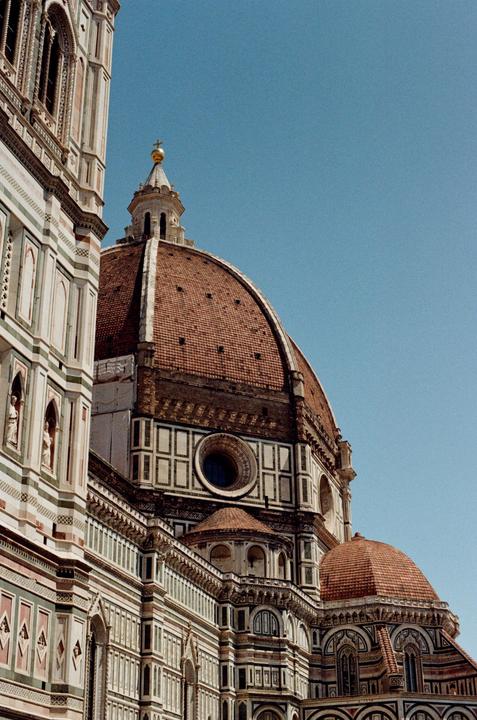 A large domed cathedral with intricate architectural details stands against a clear blue sky.
