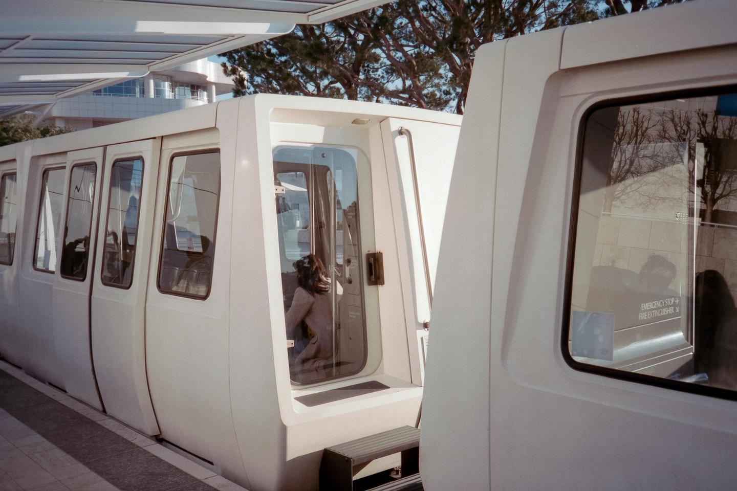 A person sits inside a white train car with an open door at a station platform.