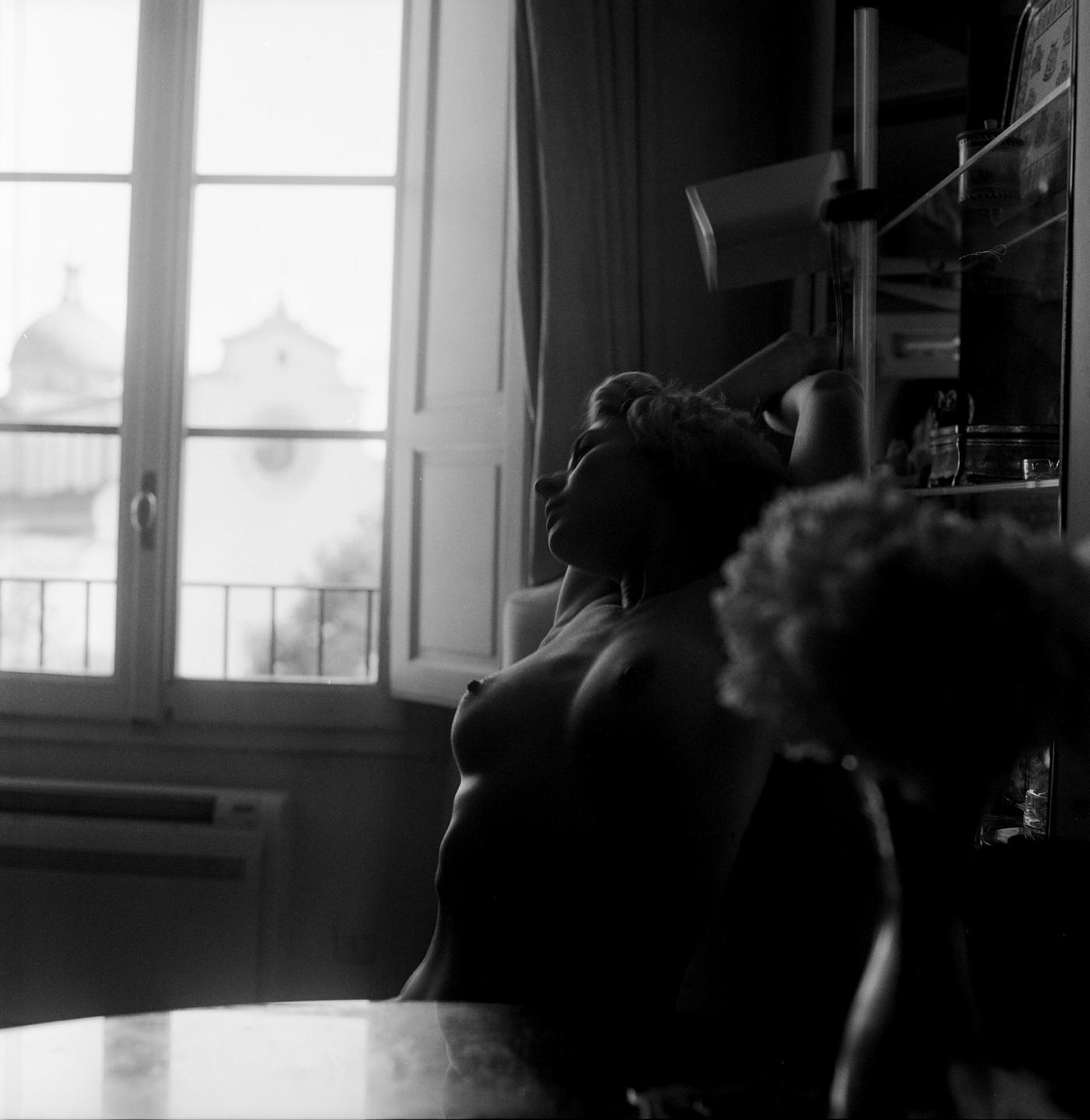 A woman is sitting in a room with a window looking out onto a building with a dome.