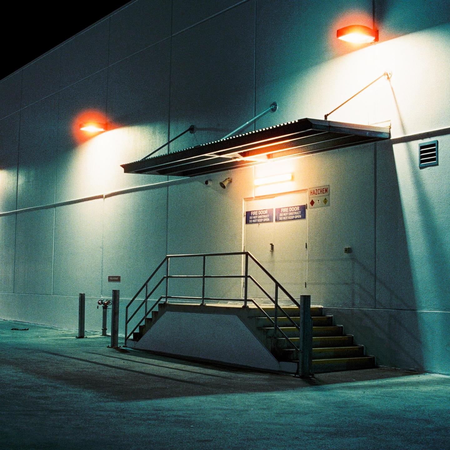 A building with a fire door and a staircase is illuminated by orange and white lights at night.