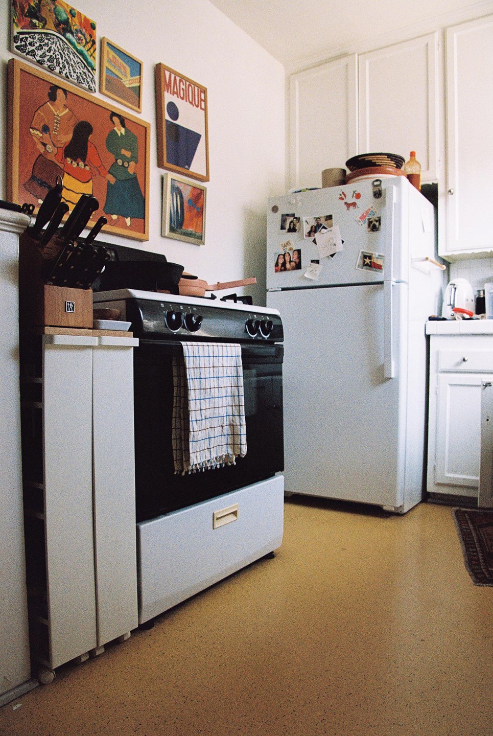A kitchen with a white refrigerator, a black oven, and several framed pictures on the wall.