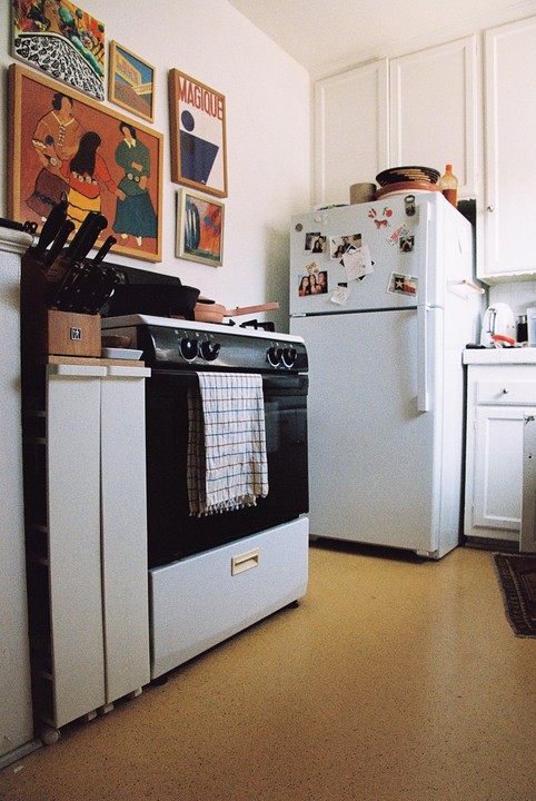 A kitchen with a white refrigerator, a black oven, and several framed pictures on the wall.
