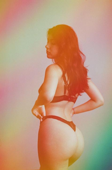 A woman in lingerie is captured from behind, looking over her shoulder with colorful light.