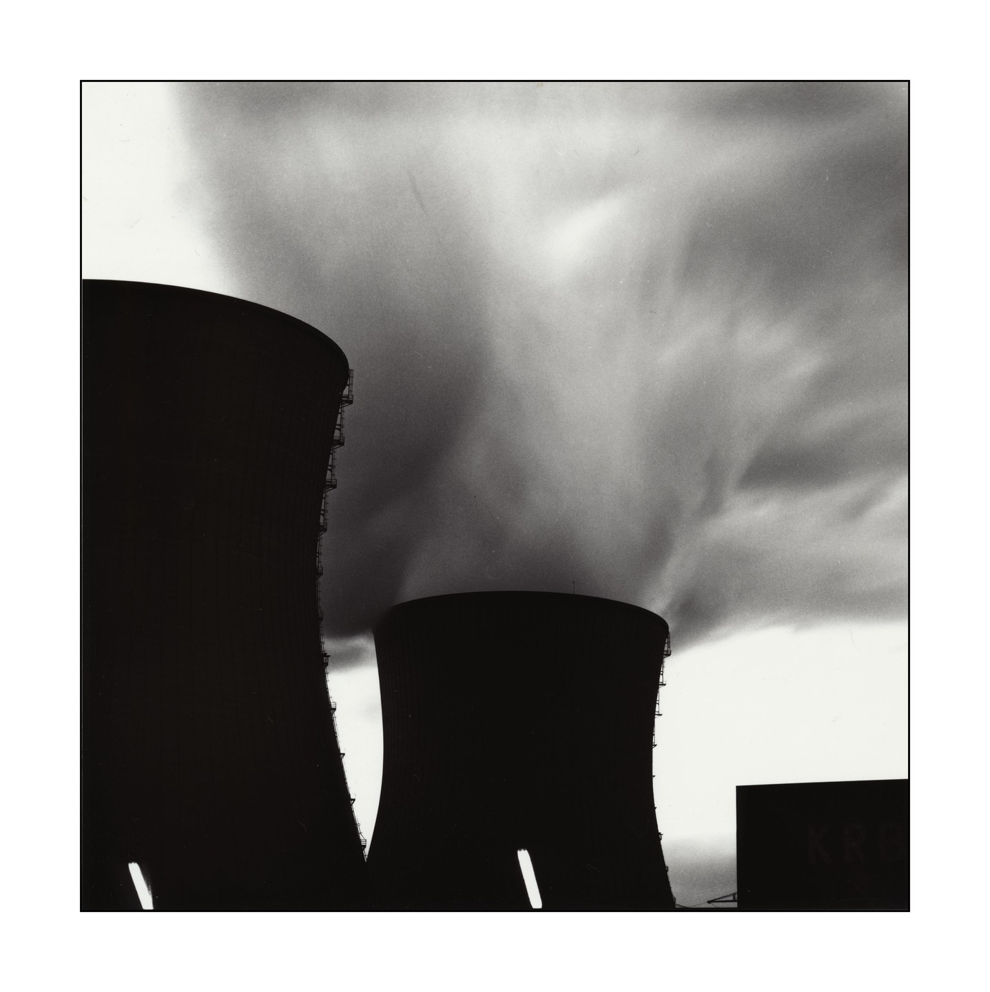 Two cooling towers emit large plumes of smoke into a cloudy sky.