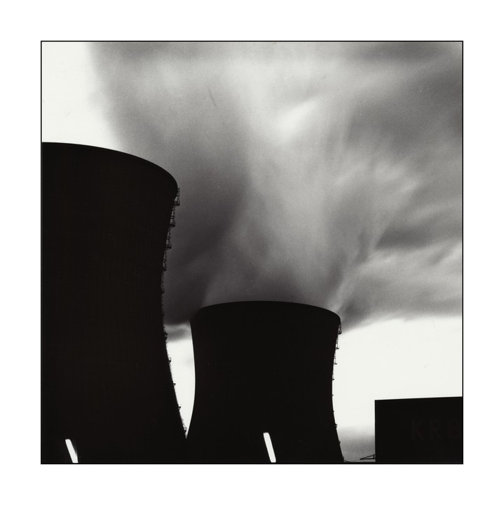 Two cooling towers emit large plumes of smoke into a cloudy sky.