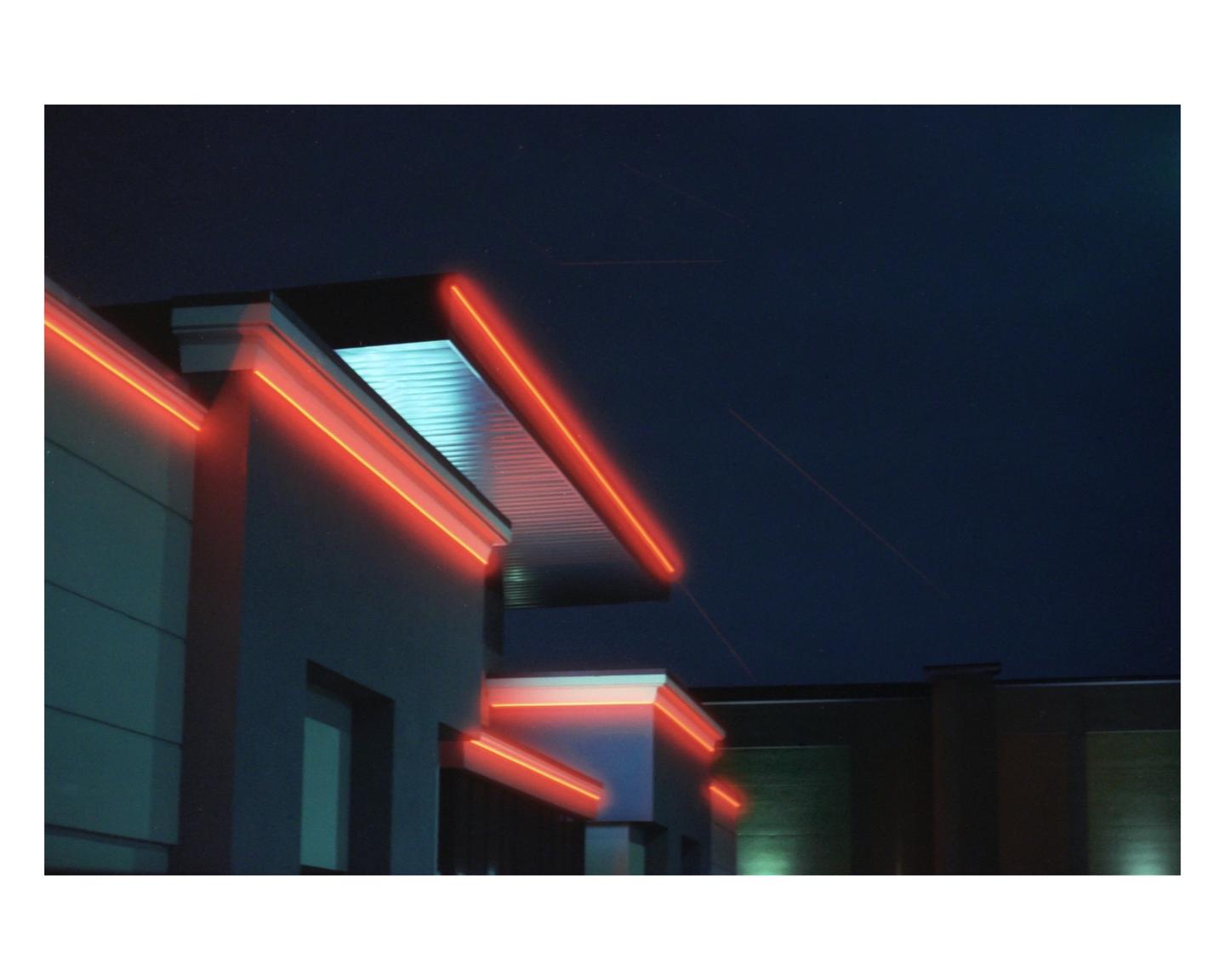 Red neon lights illuminate the edges of a building against a dark night sky.