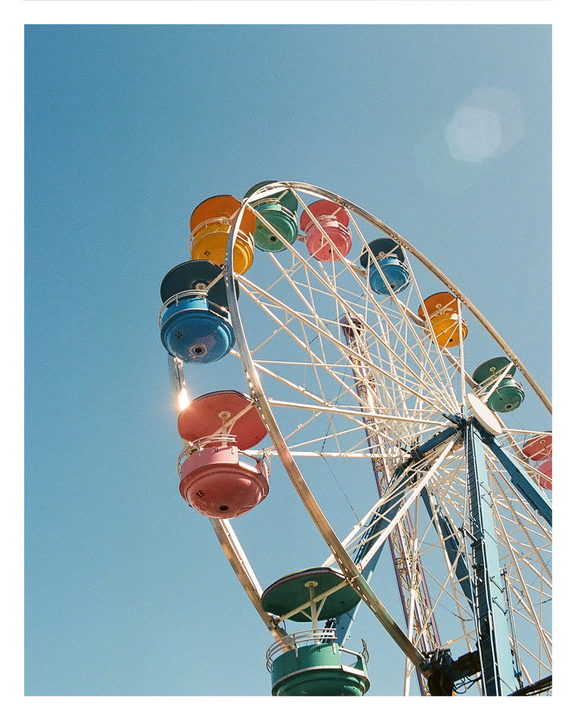 A colorful ferris wheel with pastel gondolas stands against a clear blue sky.