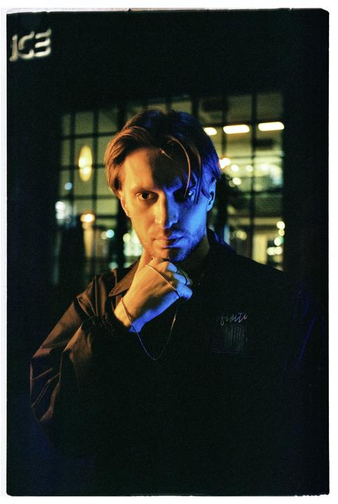 A man with a chain around his neck poses for a portrait at night with neon light.