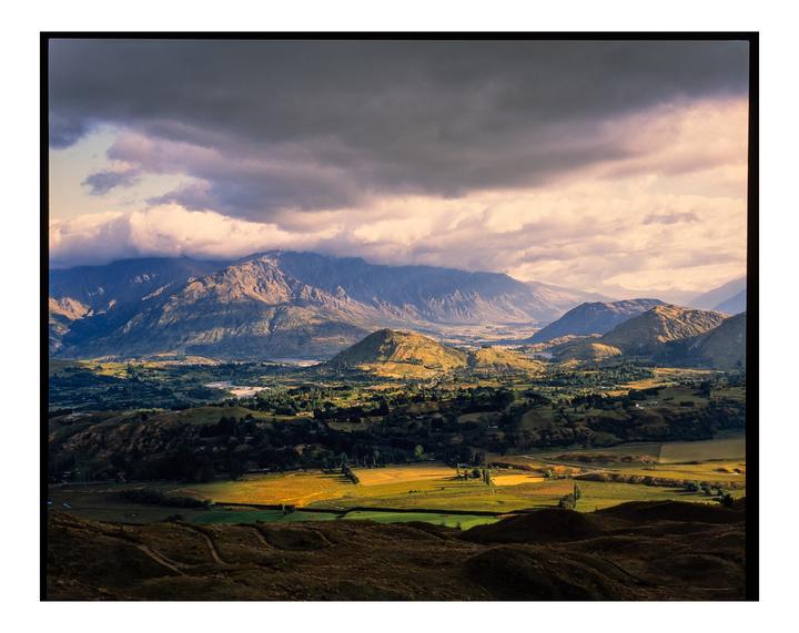 A dramatic landscape shows mountains and valleys under a cloudy sky with patches of sunlight.