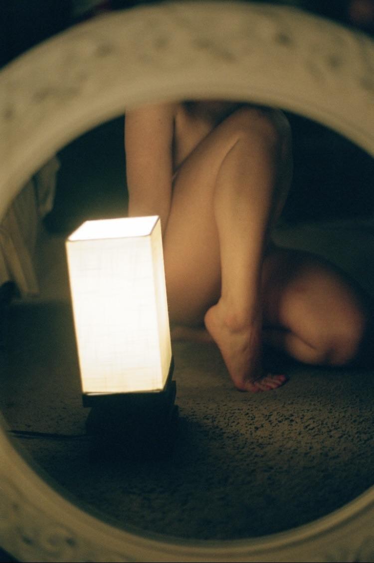 A person's legs are visible next to a glowing rectangular lamp, reflected in a mirror.