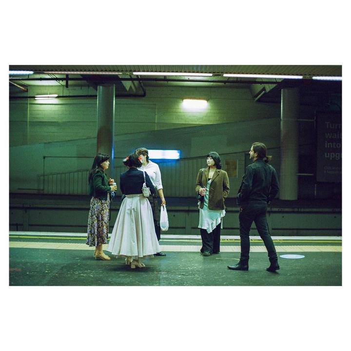 Five friends stand on a subway platform at night.
