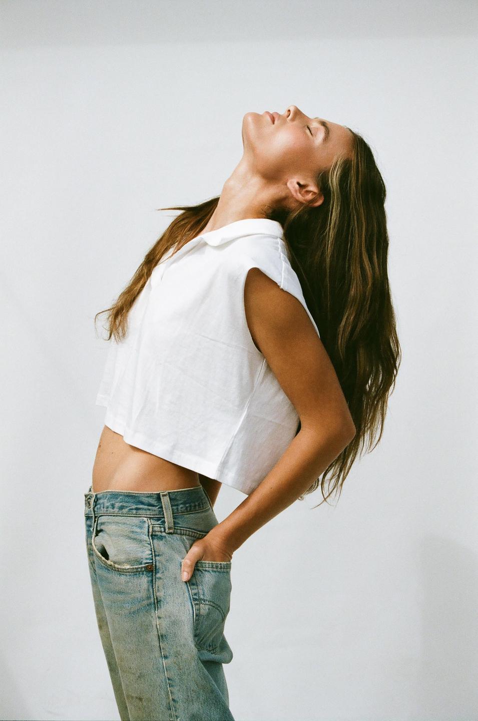 A woman with long hair and a white crop top leans back with her eyes closed.