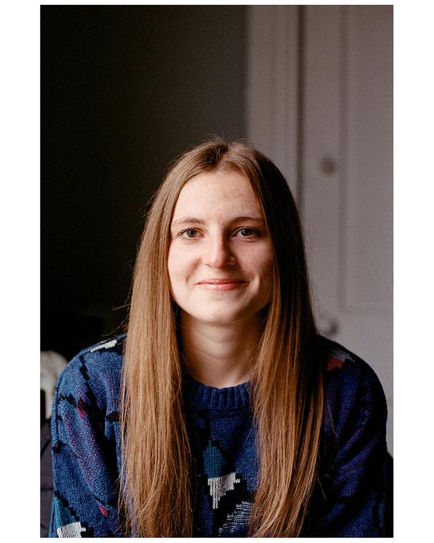 A woman with long hair and a patterned sweater smiles at the viewer.