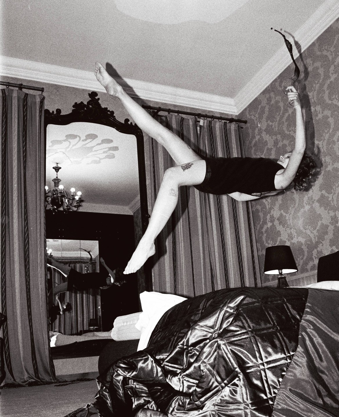 A woman floats horizontally in a hotel room, spilling a drink.