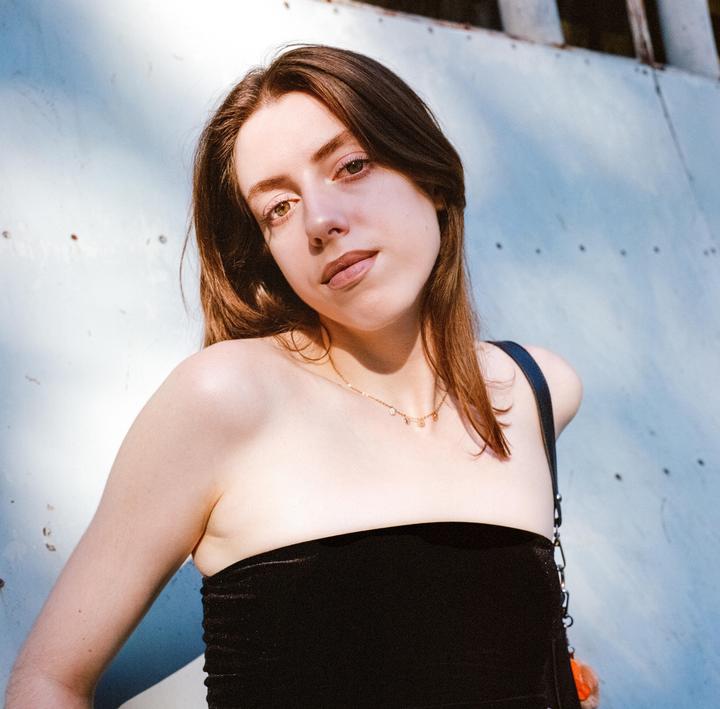 A woman with long brown hair and a black strapless top looks directly at the viewer.