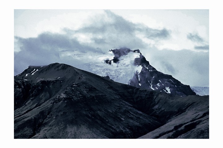 A snow-capped mountain peak is partially obscured by clouds, with dark mountain ridges in the foreground.
