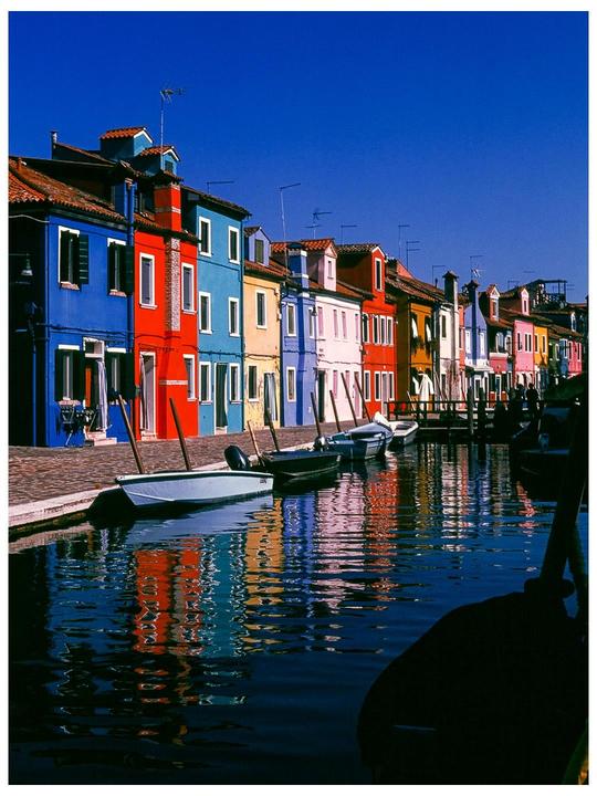 A canal with colorful houses and boats is visible under a clear blue sky.