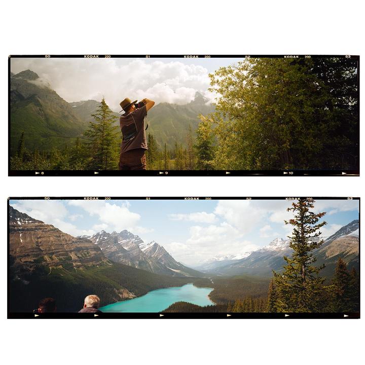 A man photographs a mountain landscape, and two people look out over a turquoise lake surrounded by mountains.