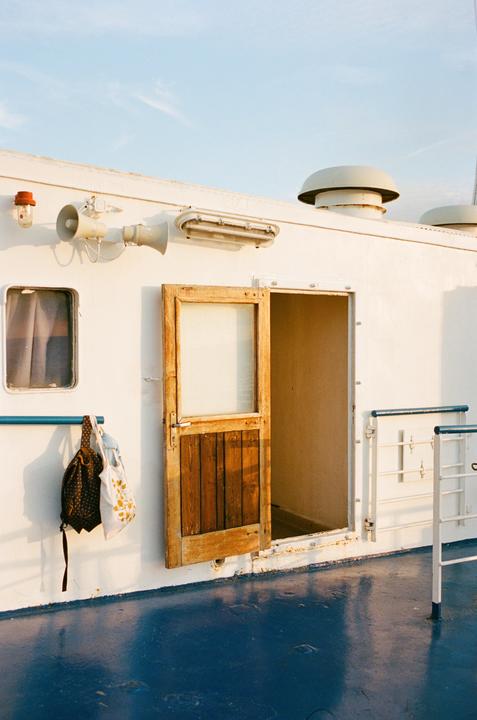 A wooden door is open on the side of a white boat with a blue deck.