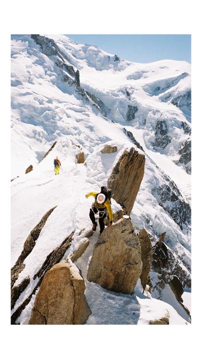 Two men are climbing a snowy mountain with exposed rock faces.