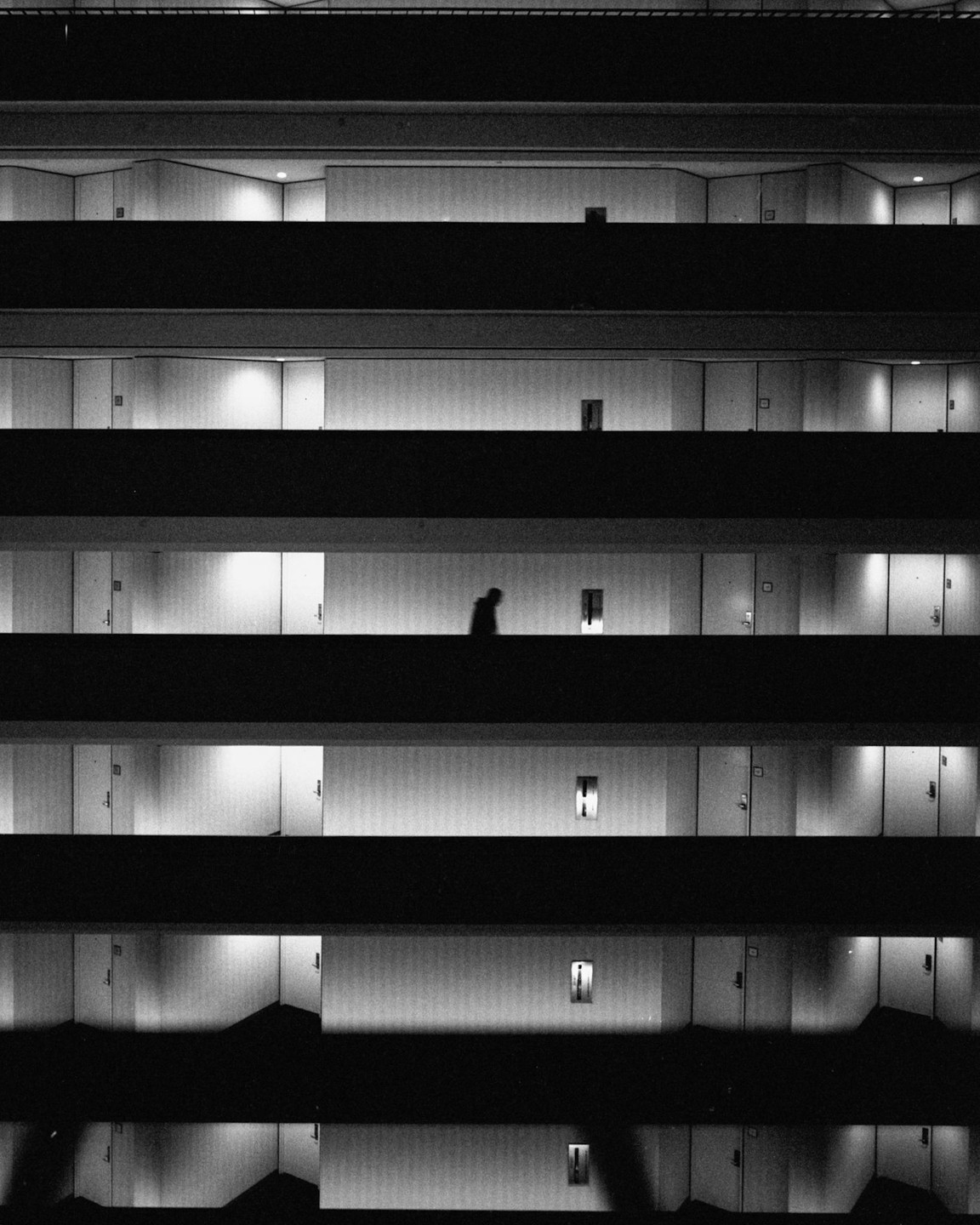 A person walks along a brightly lit hallway in a multi-story building at night.