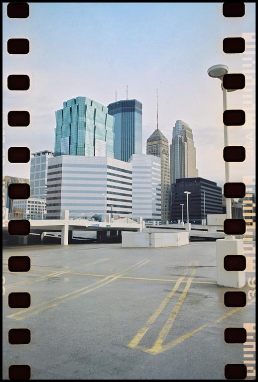 A city skyline with several tall buildings is visible from an elevated concrete parking lot.