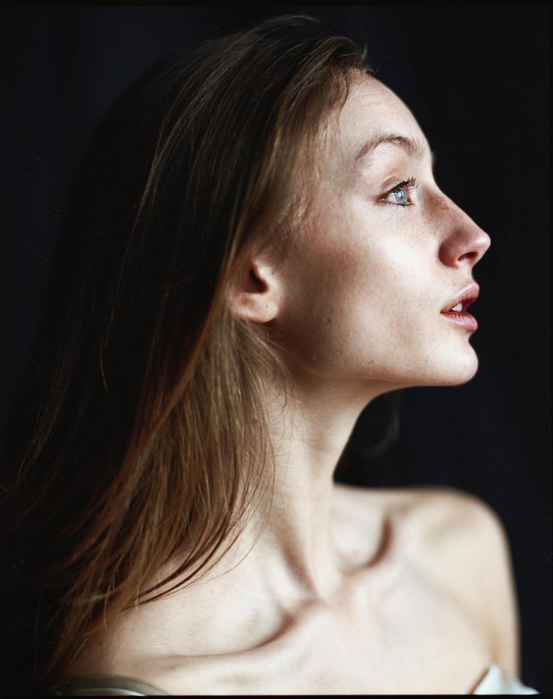 A woman with long hair looks up and to the right, her profile visible against a dark background.