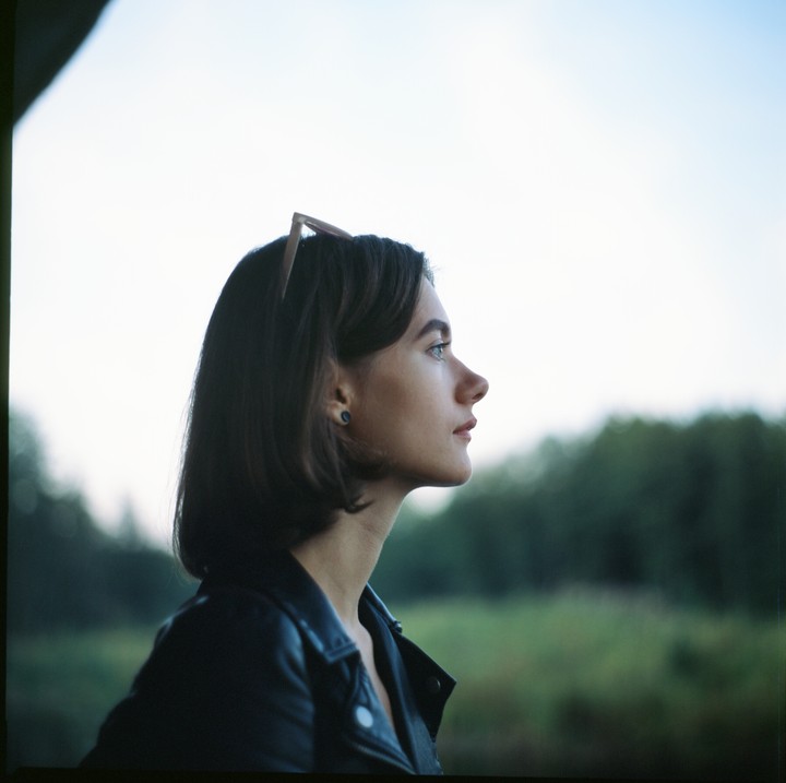 A woman in a leather jacket looks to the right with sunglasses on her head.