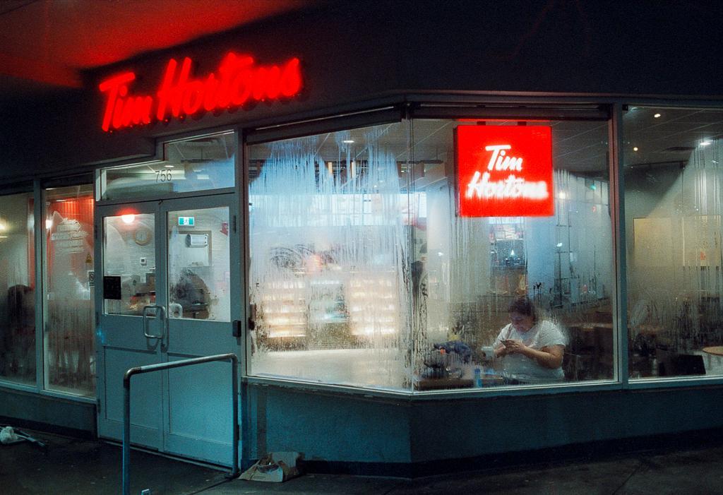 A woman sits inside a Tim Hortons at night, visible through a steamy window.