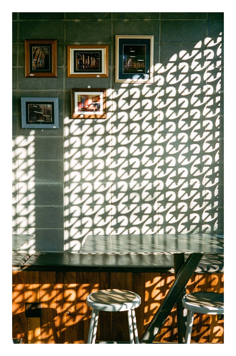 Sunlight creates a star pattern shadow on a wall with framed pictures above a table and stools.